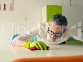 Middle-aged man thoroughly cleans a white dining room table