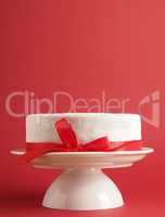 A white wedding or birthday cake with a red bow on a white cake
