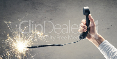 Businessman holds a telephone handset with a burning telephone c