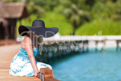 Maldives, a young woman sitting on a bridge in a black hat