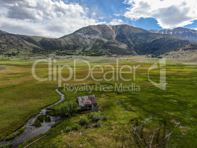 Aerial view of abandoned little wooden house barn next small river in the green valley, Aspen Spring