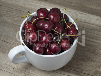 Fresh ripe cherries in a cup, on wooden background.