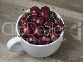 Fresh ripe cherries in a cup, on wooden background.