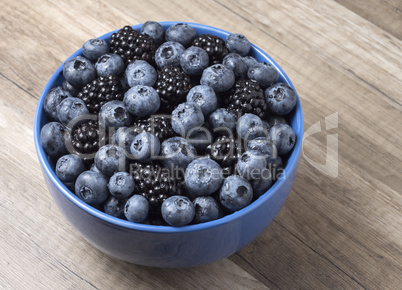 Bowl full of fresh blackberries and blueberries on a wooden back