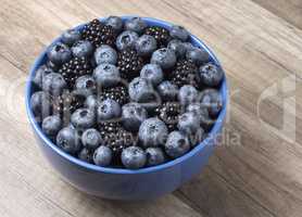 Bowl full of fresh blackberries and blueberries on a wooden back