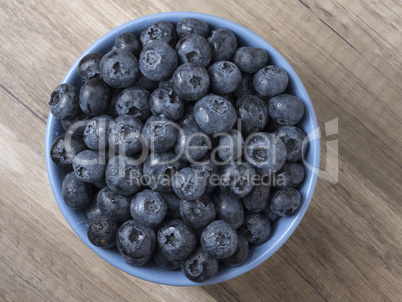 Bowl full of fresh ripe blueberries on a wooden background.