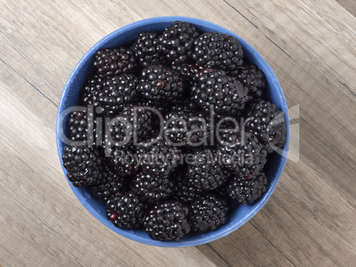 Ripe fresh blackberries in a bowl on a wooden table. Top view.