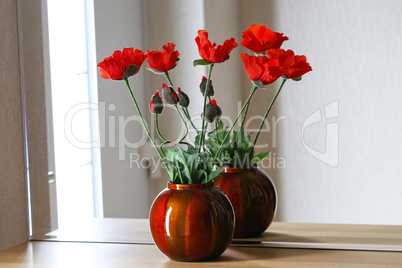 Decorative red poppies stand on a shelf with a mirror