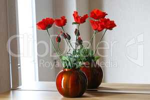 Decorative red poppies stand on a shelf with a mirror