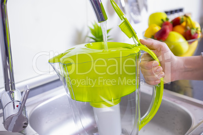Woman filling water filter jug in the kitchen