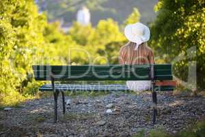 A girl in a white hat sits on a park bench