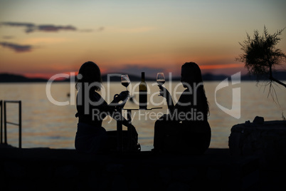 Silhouettes of girls drinking wine on the beach at sunset
