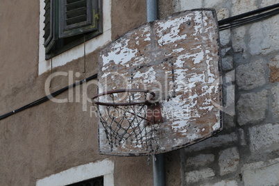 Old basketball ring is attached to the wall of the house