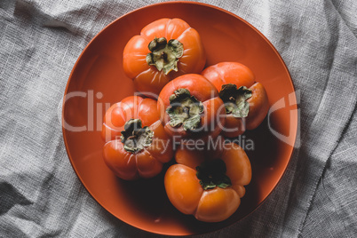 Few fresh persimmons on orange plate