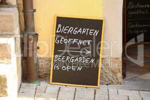 Plaque on the street. Text in German and English: Beergarden is open.