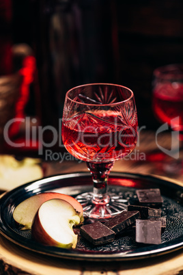 Glass of homemade redcurrant nalivka with apple slices and chocolate
