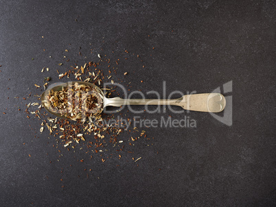 Organic tea blend on a rustic spoon, dark stone background