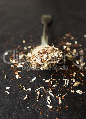 Organic tea blend on a rustic spoon, dark stone background