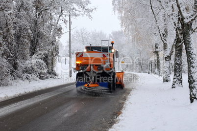 Snow plow is sprincling salt or de-icing chemicals on pavement in city.