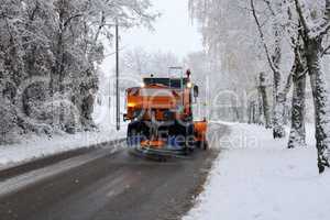 Snow plow is sprincling salt or de-icing chemicals on pavement in city.