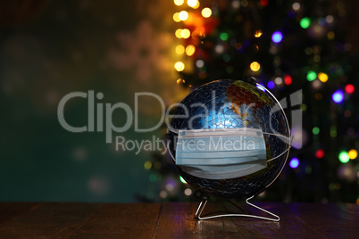 Globe in a medical mask on the background of the Christmas tree