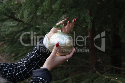 Girl hangs a beautiful Christmas ball on a fir tree in the forest