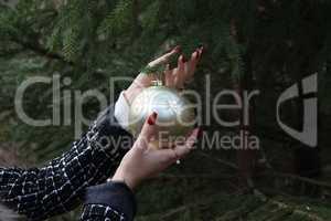 Girl hangs a beautiful Christmas ball on a fir tree in the forest