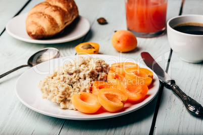 Porridge with apricot, coffee, glass of juice and croissant