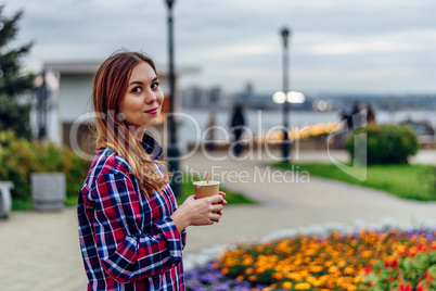 Beautiful young woman holding coffee cup and smiling in the park