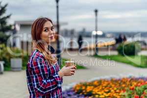 Beautiful young woman holding coffee cup and smiling in the park