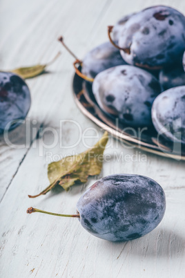 Plums on wooden surface with leaves