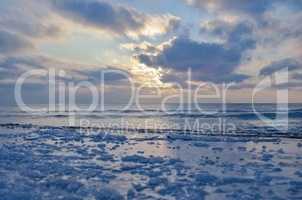 The frozen shore is covered with ice on the background of the sunset by the sea. Cold natural background