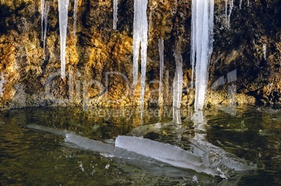 A huge icicle hanging from a rock with moss, which melts and drips into the water