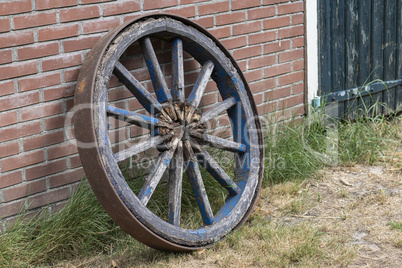 Old wooden cart wheel against a brick wall.
