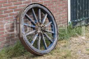Old wooden cart wheel against a brick wall.