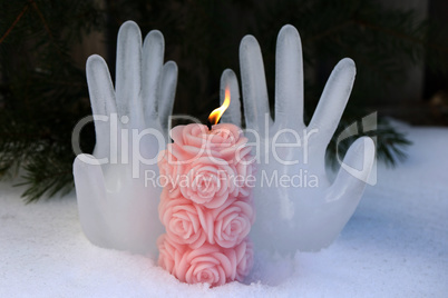 Burning candle on the background of hands made of ice