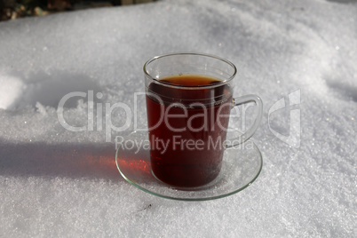A mug of hot tea stands in the snow