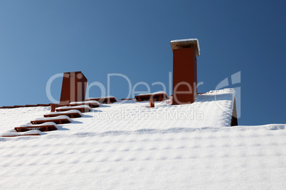 The roof with a chimney is covered with snow in winter