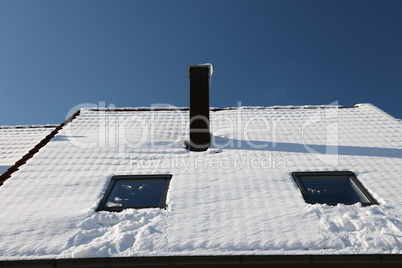 The roof with a chimney is covered with snow in winter