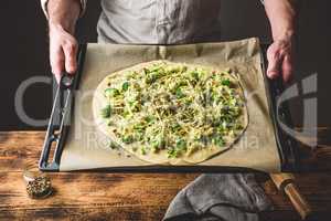 Man holding uncooked pizza with broccoli and cheese