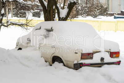 City street after blizzard. Stuck cars under the snow and ice. Buried vehicle in snowdrift on the road. Parking lots in winter after heavy snowfall. Uncleaned roads. Record-breaking amounts of snow.