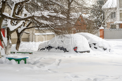 City street after blizzard. Stuck cars under the snow and ice. Buried vehicle in snowdrift on the road. Parking lots in winter after heavy snowfall. Uncleaned roads. Record-breaking amounts of snow.