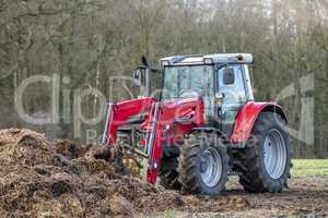 Red tractor with front loader in front of a manure heap