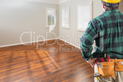 Contractor Wearing Toolbelt and Hard Hat Facing Empty Room with