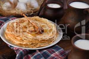 A stack of thin pancakes with honey on a wooden board.