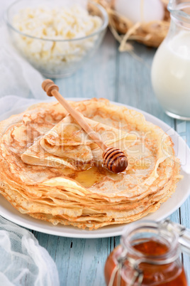 A stack of thin pancakes with honey