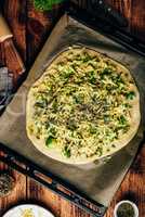Raw homemade pizza with broccoli, pesto and cheese