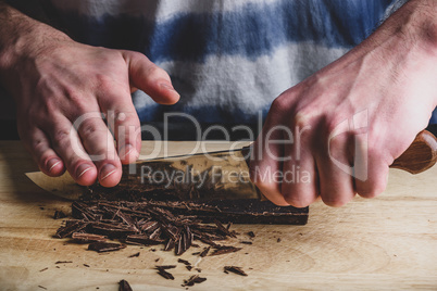 Chopping dark chocolate bar with knife