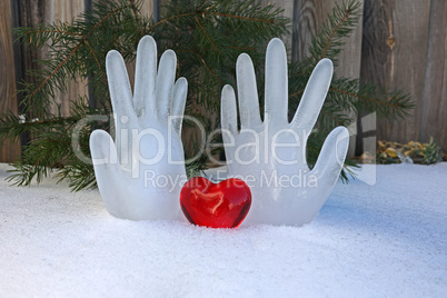Decorative heart on the snow on a background of ice hands