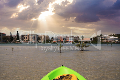 Sun shines through the clouds over a Green Kayak in the water of